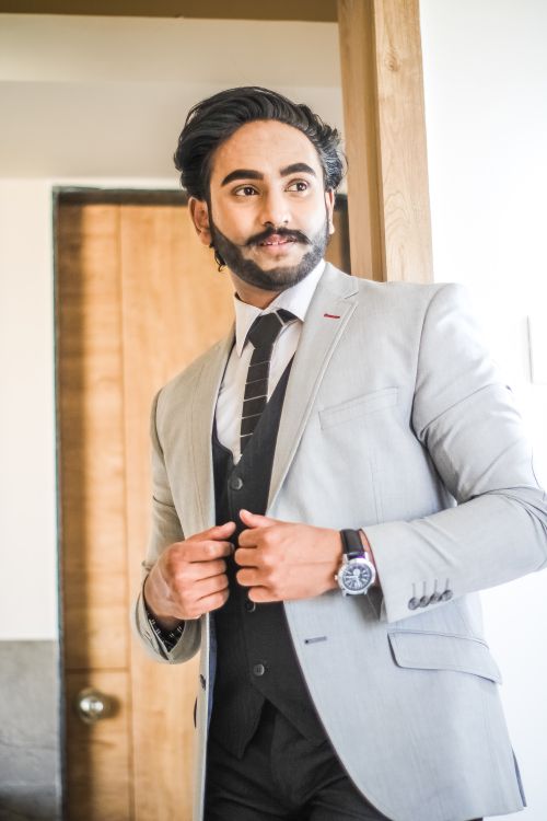 Free Confident businessman wearing a gray blazer and tie, posing indoors near a wooden door. Stock Photo