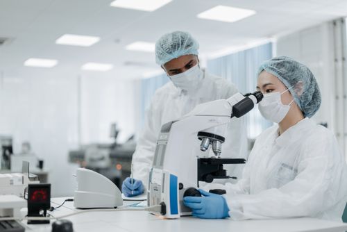 Free Scientists in protective suits examining samples under a microscope, focusing on microbiological research. Stock Photo