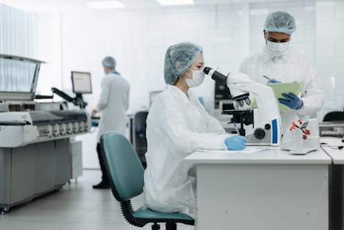Free Woman in White Protective Suit Looking Through Microscope Stock Photo