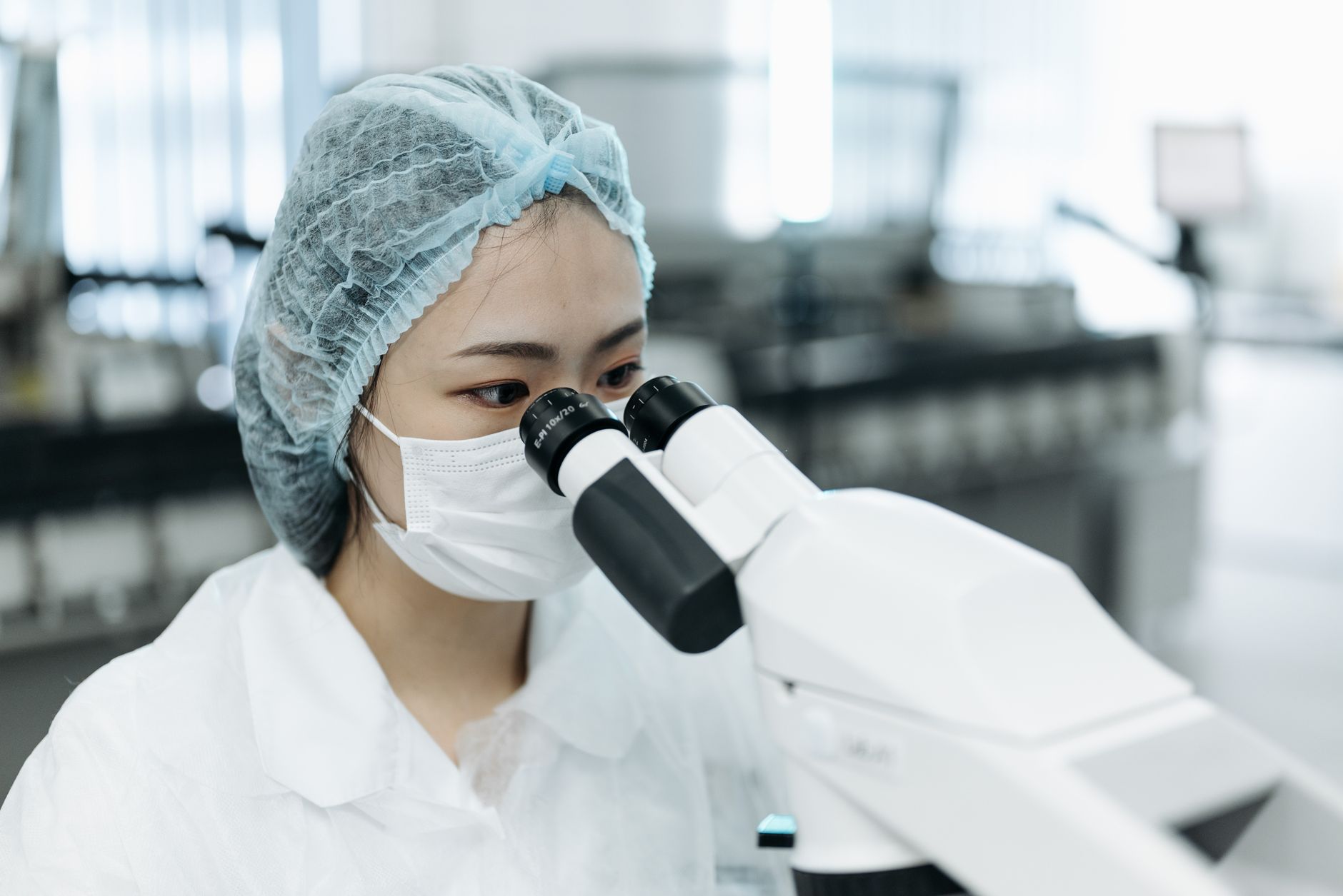 A female scientist in protective clothing examines samples using a microscope in a modern laboratory.