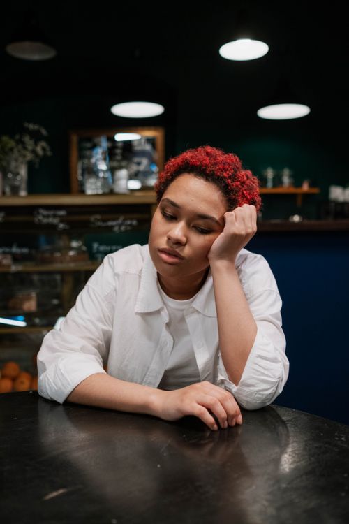 Free Woman with red hair sits thoughtfully at a cafe table under soft lighting. Stock Photo