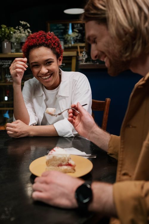 Free A smiling couple shares a slice of cake at a cozy café. The mood is warm and inviting. Stock Photo