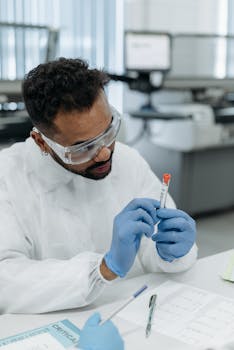 Scientist wearing protective gear examines test tube in lab environment.
