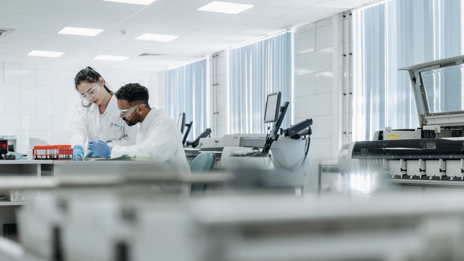 Two scientists working in a high-tech laboratory setting, wearing protective eyewear and gloves.