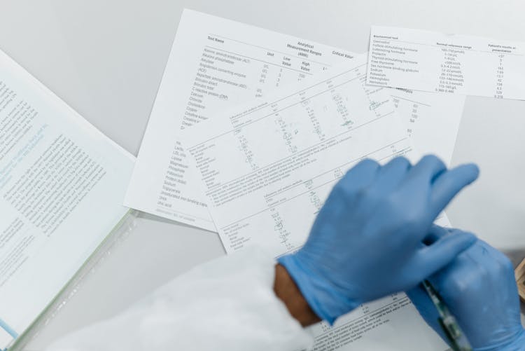 Person Wearing Latex Gloves Over Paperwork On A White Surface