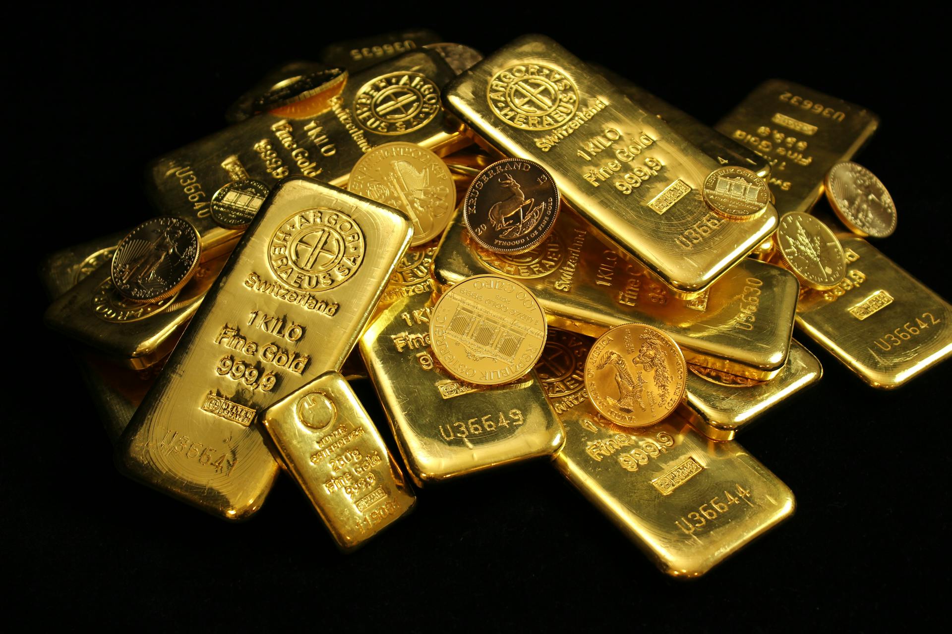 A close-up of gold bars and coins symbolizing wealth and investment on a black background.