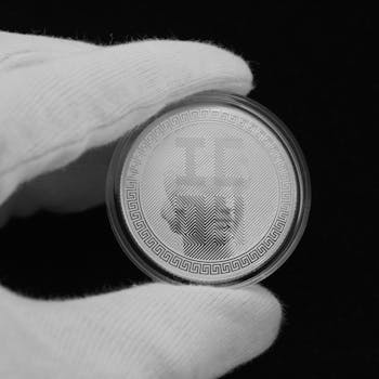 Close-up view of a silver coin held in a gloved hand on a black background.