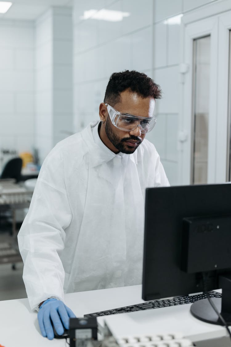 A Man In Lab Gown Working On The Lab Computer