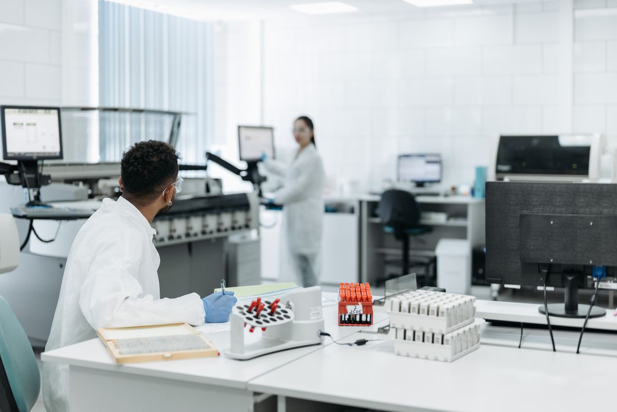 Two lab scientists at work in a bright lab with analyzers and racks of samples