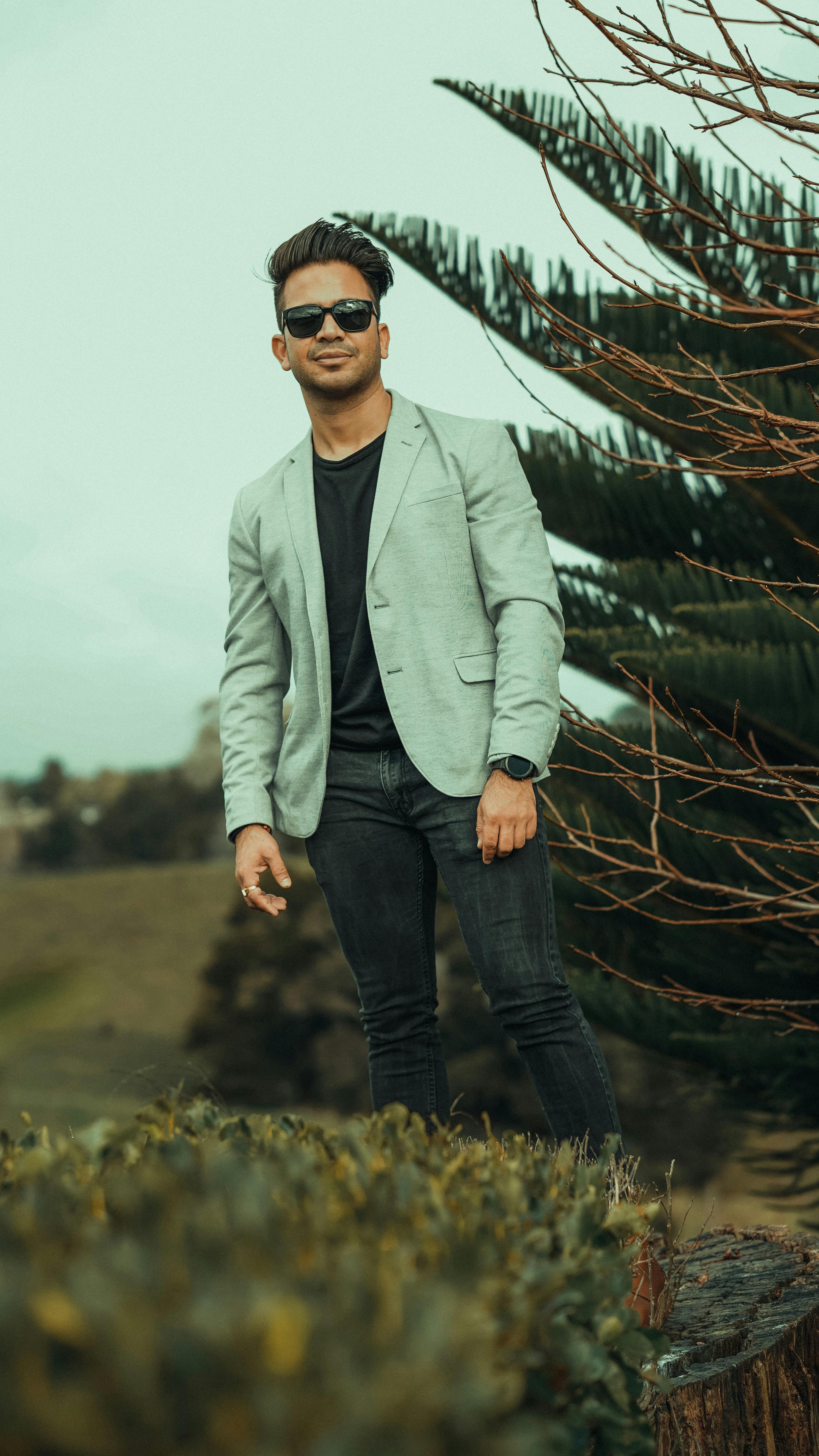 Confident man in blazer and sunglasses, posing outdoors with a smile.