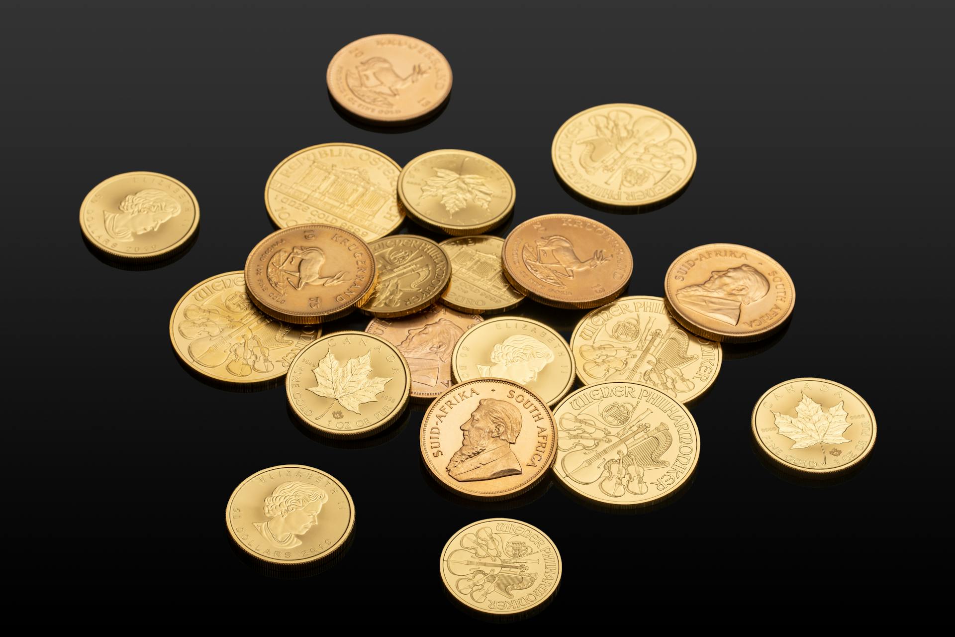 Close-up of various international gold coins on a reflective black surface, showcasing global currency.