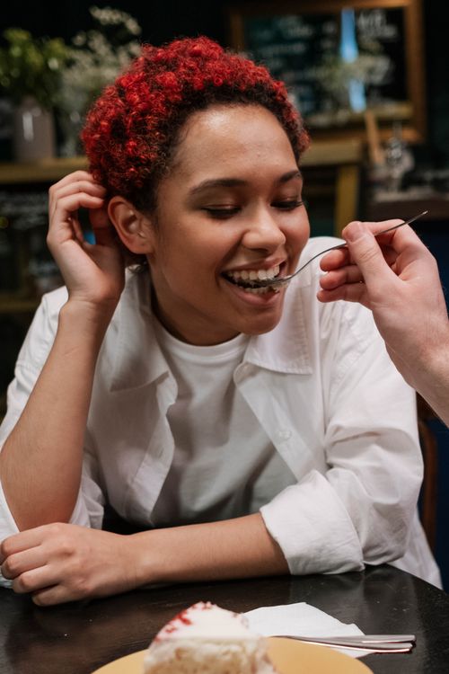 Free Smiling woman with red hair being fed dessert indoors, spreading happiness. Stock Photo