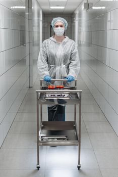 Scientist in protective gear handling lab equipment in a sterile hallway.
