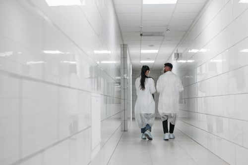 Free Two scientists in lab coats walk down a bright, tiled hallway, showcasing modern research environment. Stock Photo