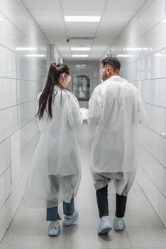 Researchers in lab coats and goggles walking through a laboratory hallway, engaging in teamwork.