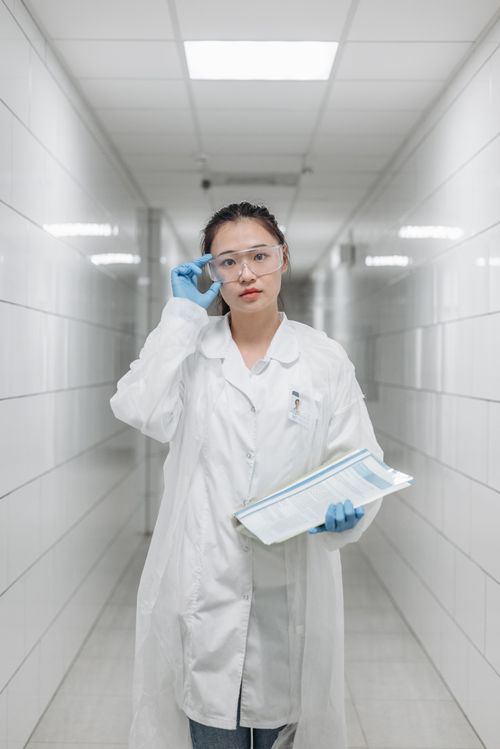 Free A woman scientist wearing a lab coat and goggles stands in a bright laboratory hallway. Stock Photo