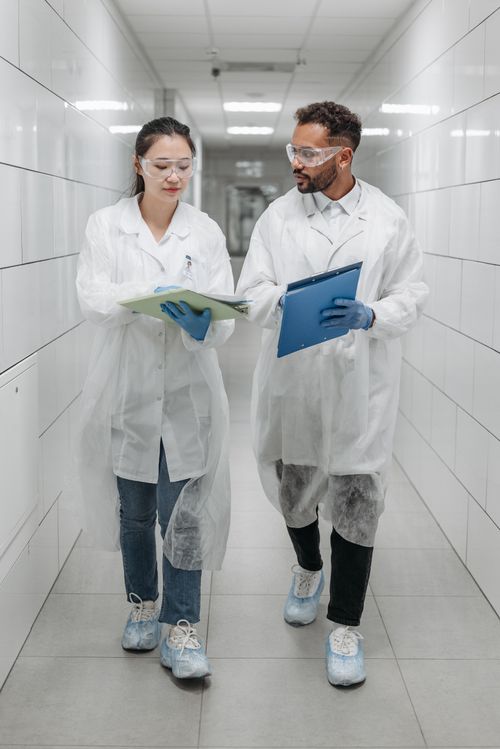 Free Two scientists in lab coats discussing research documents in a laboratory hallway. Stock Photo