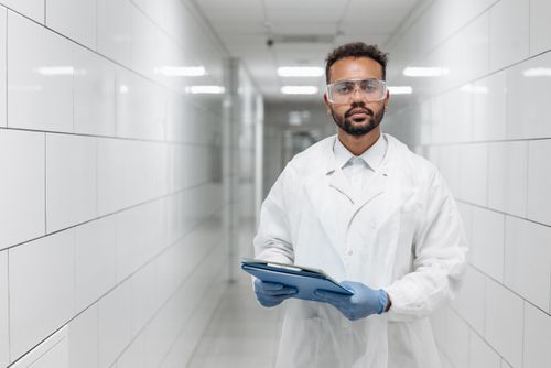 Free Portrait of a scientist in a laboratory hallway wearing protective goggles and gloves. Stock Photo