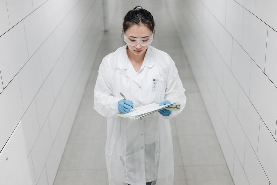 A female scientist wearing safety goggles and a lab coat taking notes in a laboratory corridor.