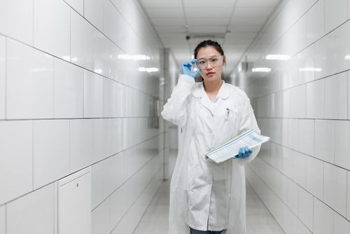 Free Asian female scientist walking in a laboratory corridor with protective goggles and a lab coat. Stock Photo