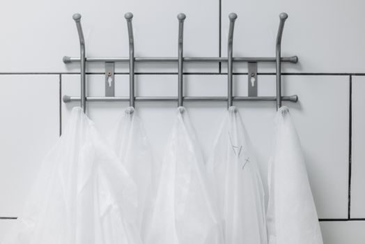 White lab coats hanging on a metal wall hook in a sterile laboratory environment.