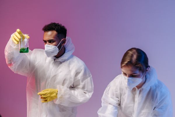 Scientists wearing protective gear in lab, analyzing chemical in flask.