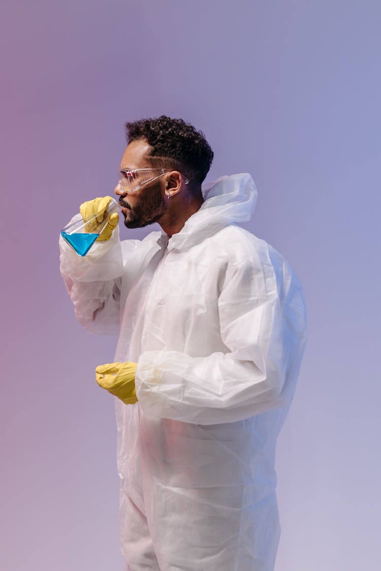 Male Scientist In Personal Protective Equipment Smelling A Research Sample From A Beaker