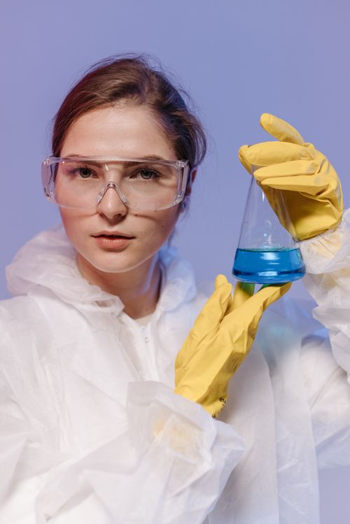 Free A female scientist in protective gear holding a beaker with blue liquid in a laboratory setting. Stock Photo