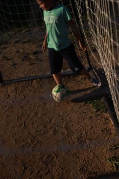 A young boy playing soccer outdoors, skillfully maneuvering the ball on a dirt field, captured from above.