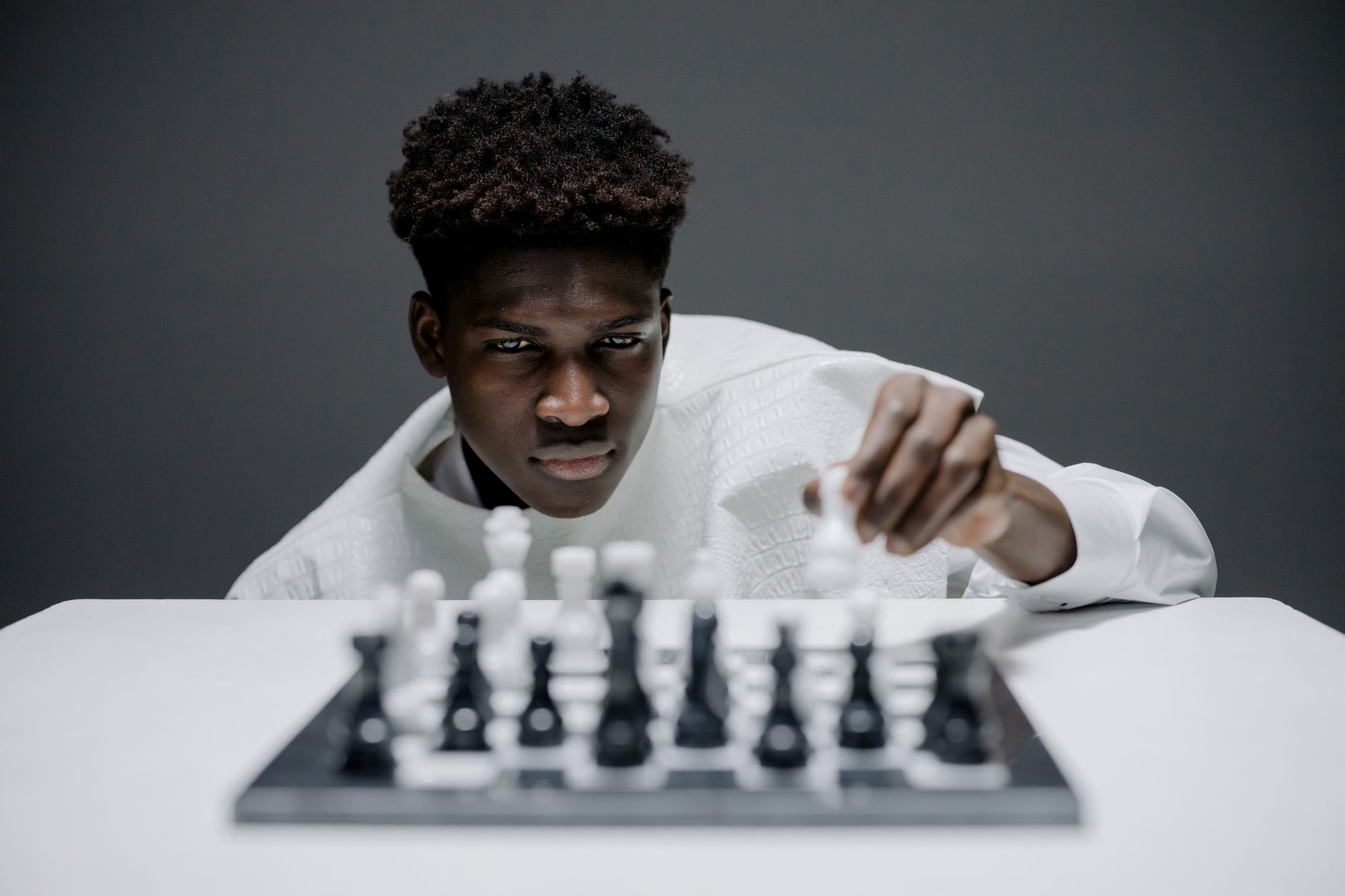 Young man in white playing chess indoors, demonstrating concentration and strategy.