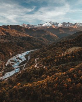 A breathtaking aerial view of the Teberda river winding through lush valleys and snow-capped mountains.