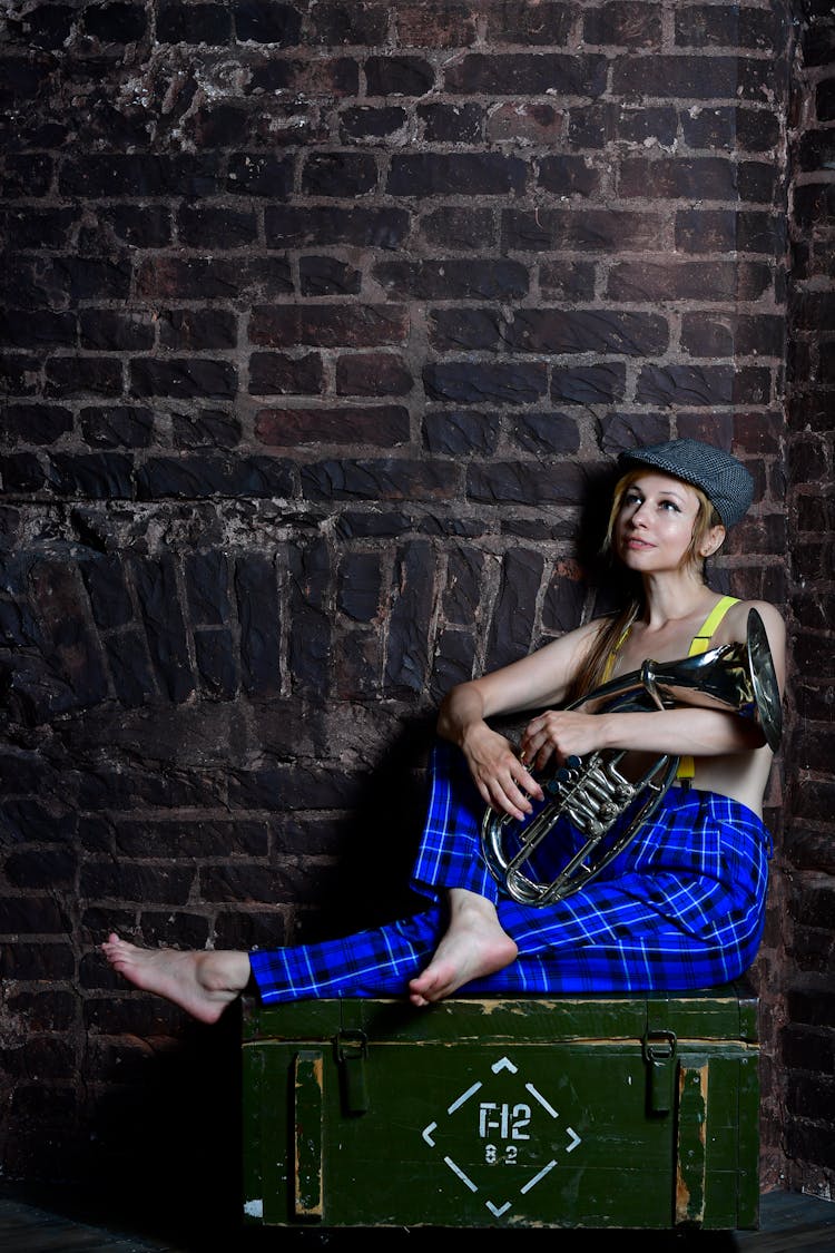 Woman Sitting On Top Of Wooden Box And Holding A Tuba 