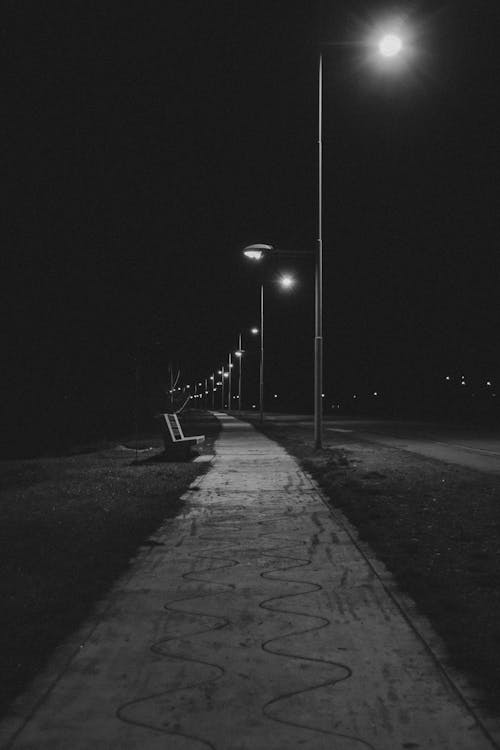 Grayscale Photo of a Sidewalk Near Lighted Street Lamps