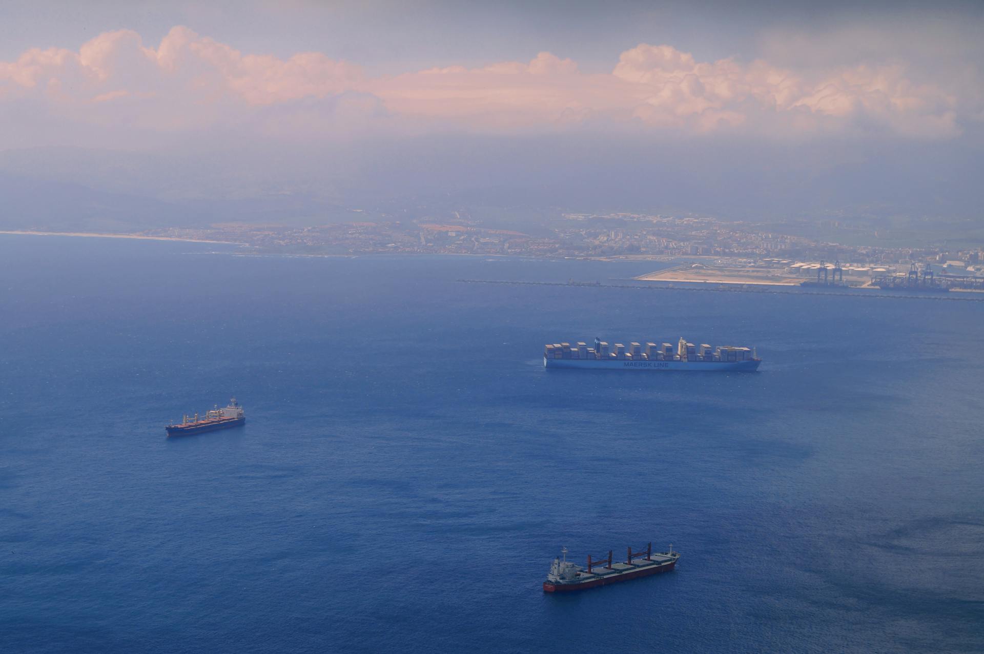 Aerial view of cargo ships navigating through the picturesque waters near Gibraltar's coastline.