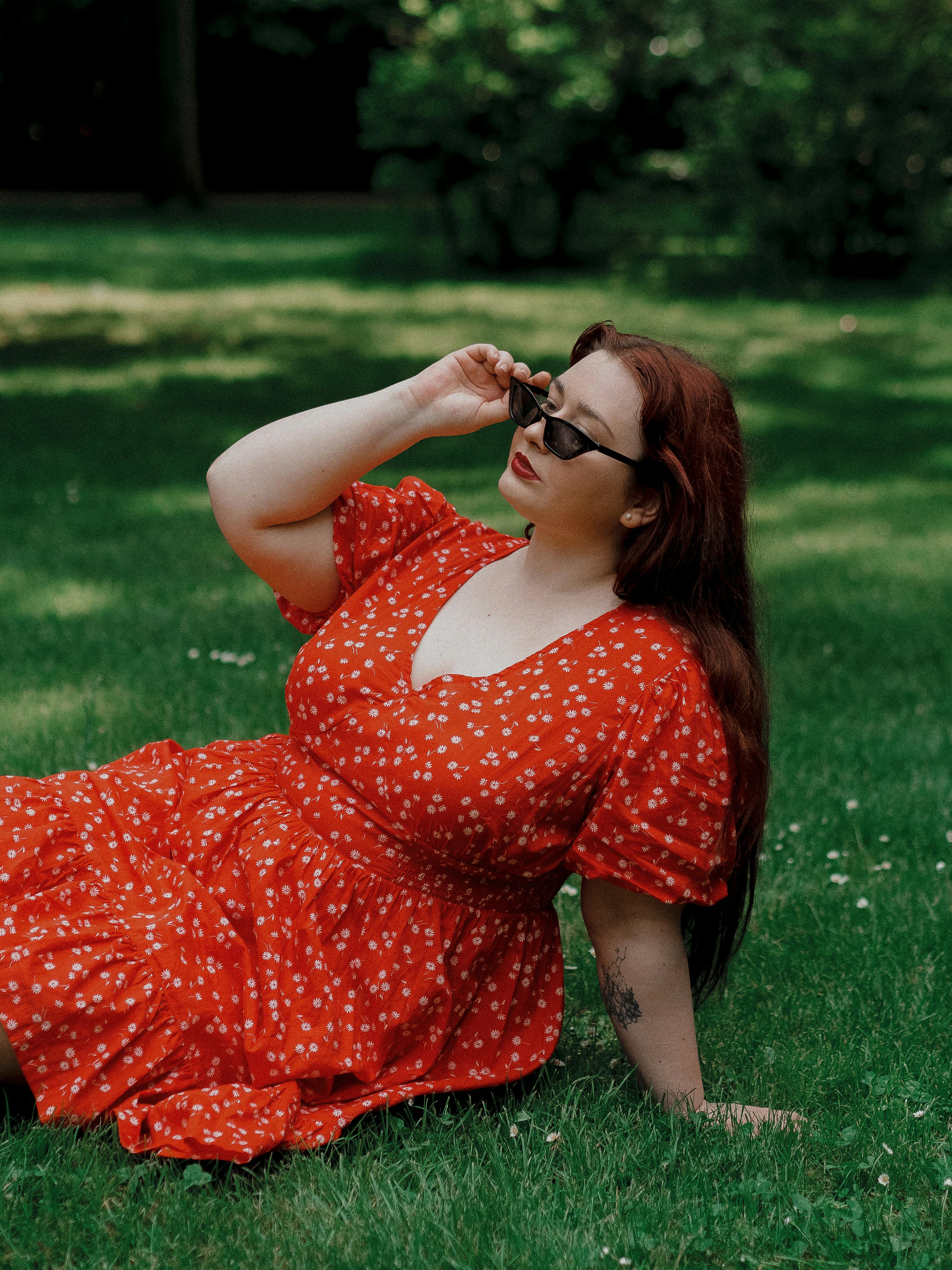 A woman in a vibrant red dress with sunglasses relaxes on a sunny day, enjoying the outdoors.