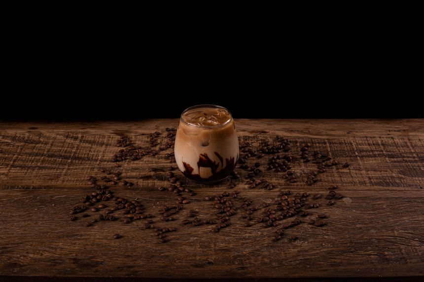 Iced coffee in a glass on a wooden counter scattered with beans — photo by Guto Macedo on Pexels