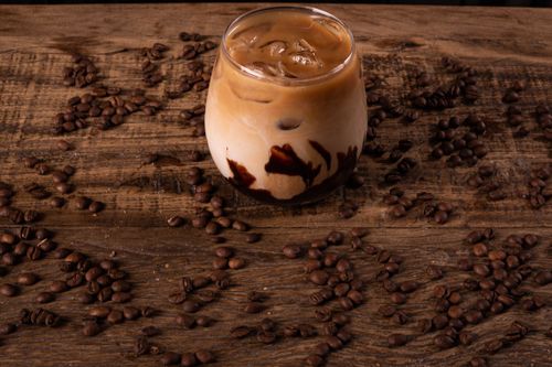 Free A cold iced coffee with chocolate syrup surrounded by coffee beans on a rustic wooden table. Stock Photo