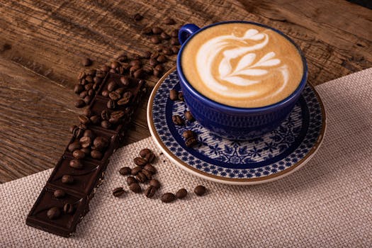 A beautifully crafted latte in a blue cup with coffee beans and chocolate on a rustic table.