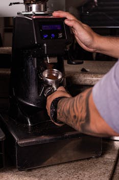 Close-up of a barista preparing espresso using a coffee grinder and portafilter in a cafe setting.