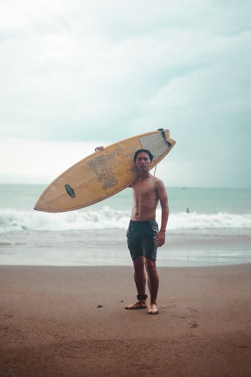 Free Man posing with surfboard on sandy beach at the seashore under cloudy skies. Stock Photo