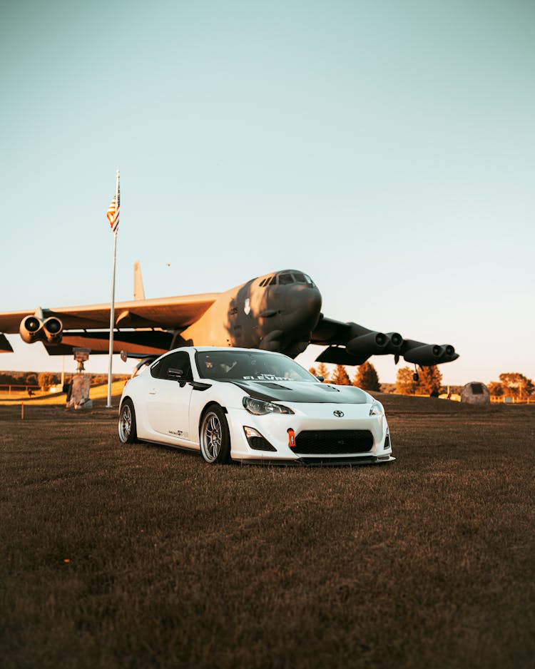 White Car Beside An Airplane On A Grass Field