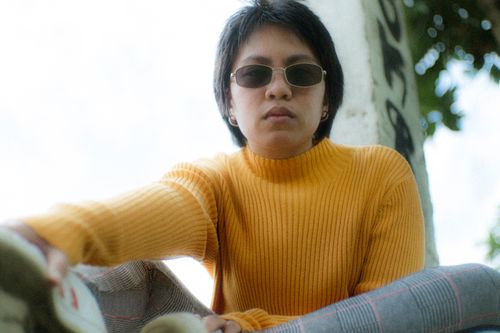Free A fashionable woman wearing sunglasses and a yellow turtleneck sweater, sitting outdoors. Stock Photo