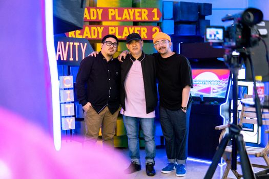 Three stylish men posing in a trendy arcade environment, showcasing modern streetwear fashion.
