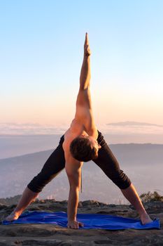 A man performing a yoga pose outside at sunrise, focusing on balance and flexibility.