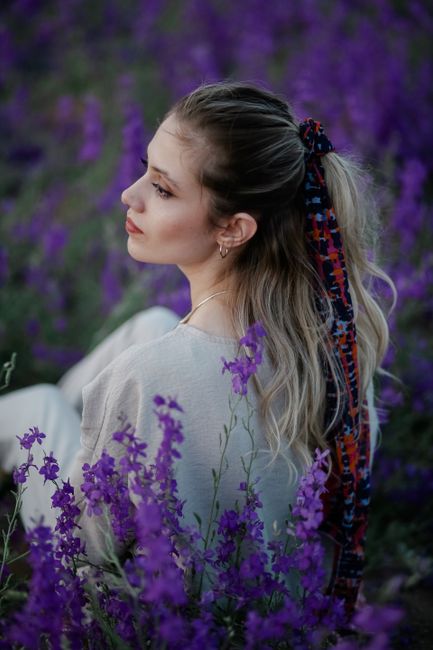 A serene portrait of a woman sitting amidst vibrant purple flowers, conveying elegance and tranquility.