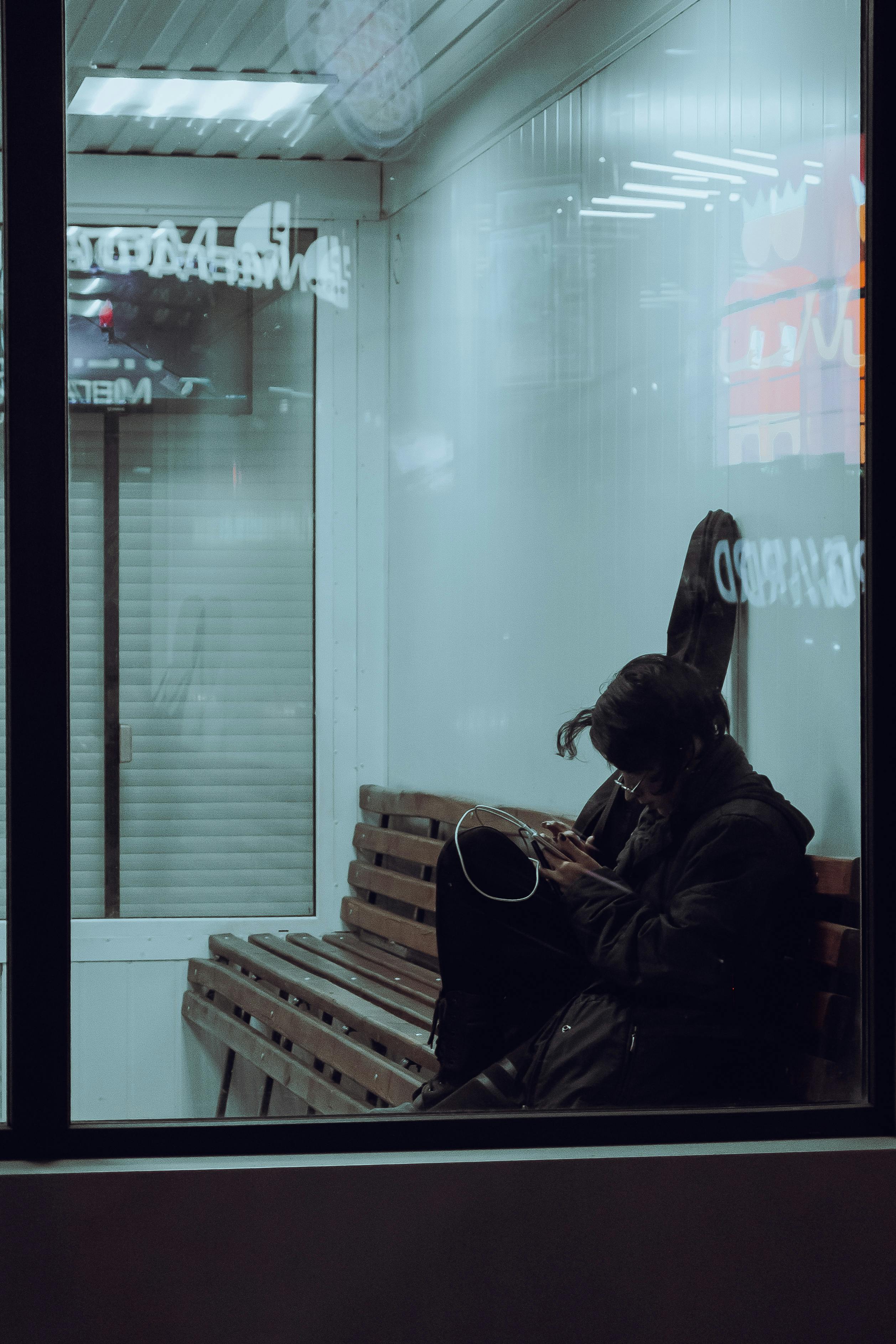 A woman sits alone on a bench inside an airport terminal, checking her phone.