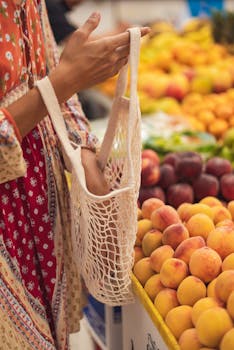 Close-up of woman's hand holding a reusable bag at a market stall filled with fresh fruits.