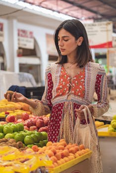 A young woman in a colorful dress selecting fruits at an outdoor market.