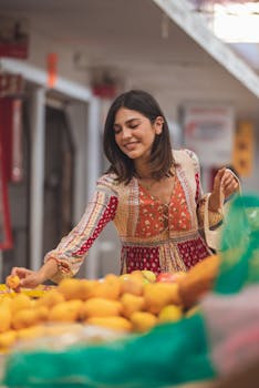 Smiling woman in printed dress shopping for fresh fruits at an outdoor market.