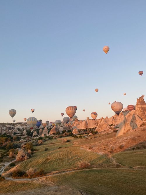 Free Scenic view of hot air balloons floating over rocky formations in Cappadocia, Turkey at sunrise. Stock Photo
